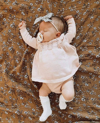 Baby in a pink outfit lying on a brown floral-patterned blanket


